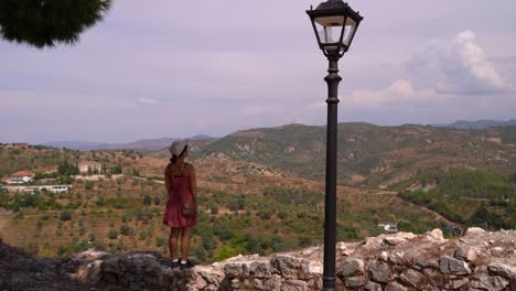 Female-tourist-standing-on-stone-wall,-looking-into-distance-at-countryside---Slow-motion-view