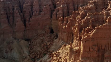Beautiful-aerial-drone-shot-tilting-down-and-approaching-the-Goblin's-Lair-cave-in-the-Goblin-Valley-State-Park-in-middle-of-the-desert-in-Utah-with-large-red-rock's-surrounding-it