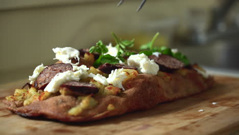 Chef-composing-a-pizza:-placing-leafy-watercress-on-top-of-a-sausage,-potato-and-mozzarella-Roman-style-pizza
