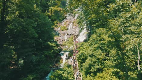 Beautiful-drone-footage-of-people-walking-on-a-bridge-alongside-a-beautiful-waterfall,-Amicalola-Falls,-the-largest-waterfall-in-all-of-Georgia