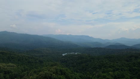 An-aerial-footage-towards-a-lush-rainforest,-mountains-in-the-horizon,-and-lake-in-the-middle-glittering-like-a-gem,-Thailand