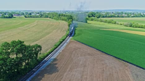 An-Aerial-View-of-a-Steam-Engine-Puffing-Smoke-and-Steam-with-Passenger-Coaches-Traveling-on-a-Single-Track-Thru-Trees-and-Farmland-Countryside-on-a-Beautiful-Cloudless-Spring-Day