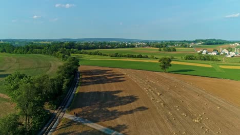 Eine-Luftaufnahme-Der-Farmlandschaft-Mit-Bepflanzten-Feldern-Und-Einer-Einzigen-Eisenbahnstrecke-In-Einer-Kurve-An-Einem-Schönen-Sonnigen-Tag