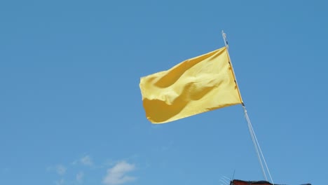 Gelbe-Fahne-Weht-Im-Wind-Gegen-Isolierten-Blauen-Himmel-Am-Strand,-Low-Angle-Shot