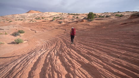 Back-of-Female-Hiker-With-Backpack-Walking-on-Rocky-Sandstone-Patterns-in-Desert-of-Utah,-Cosmic-Ashtray-Hiking-Trail,-Full-Frame-Slow-Motion