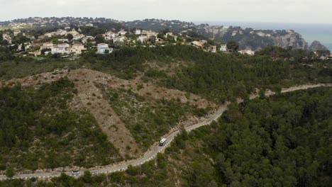 Aerial-shot-of-sparse-traffic-on-a-hillside-road-in-the-seaside-town-of-Jávea,-Spain,-on-a-cloudy-day