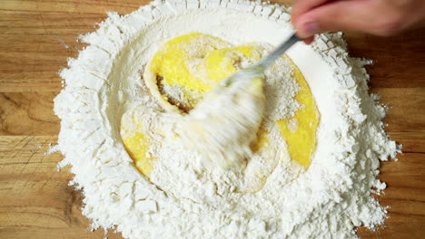 Top-view-of-pasta-making:-egg-yolks-are-beaten-inside-a-well-of-flour