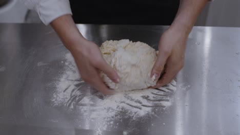 Nahaufnahme-Der-Hände-Des-Kochs,-Der-Den-Pizzateig-Aus-Der-Schüssel-Nimmt-Und-Auf-Dem-Küchentisch-Knetet
