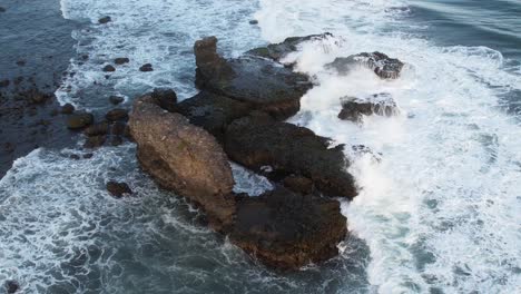 Static-Aerial-shot-of-waves-break-on-rocks-in-a-blue-ocean