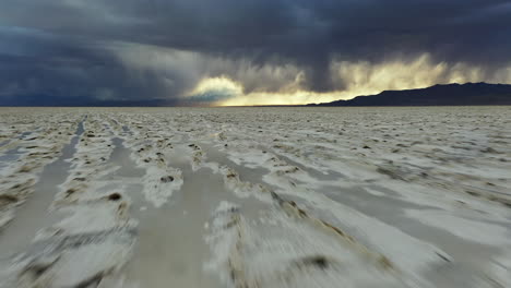 Dynamischer-Tiefflug-über-Salt-Flats,-Bonneville,-Utah,-USA,-Dramatischer-Stürmischer-Himmel-Am-Endlosen-Horizont,-Nach-Oben-Geneigter-Drohnenschuss