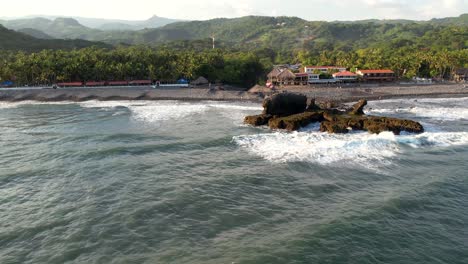 Aerial-view-of-waves-break-on-rocks-in-a-blue-ocean
