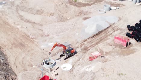 Birdseye-above-excavation-digger-vehicle-preparing-concrete-pipe-aerial-view-on-housing-development-construction-site-tilt-up