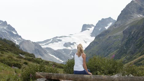 Young-sporty-woman-having-a-breake-hiking-in-the-mountains-and-enjoying-the-view-of-the-alpine-mountains-covert-with-snow