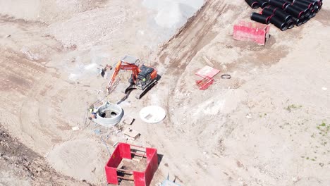 Excavation-digger-bulldozer-preparing-concrete-pipe-aerial-from-above-view-on-housing-development-construction-site-orbit-right