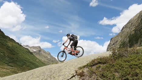 Mtb-mountain-biking-on-a-big-rock-high-up-in-the-mountains-with-beautiful-alpine-view