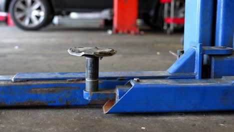 Slow-panning-right-to-left-of-distressed-blue-industrial-automotive-car-truck-lift-jack-in-mechanics-garage-shop
