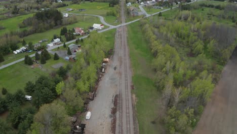 Aerial-view-from-drone-flying-over-railroad-tracks-looking-down-on-rural-farm-town-with-small-buildings,-homes-and-church-in-distance