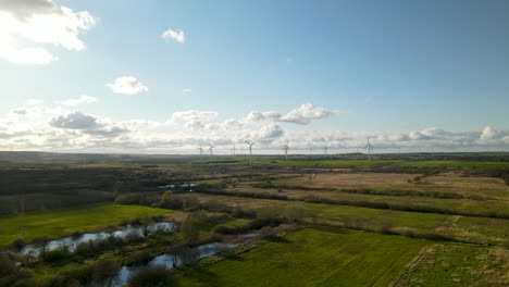 Aerial-landscape-of-wind-power-plant-surrounded-with-green-agricultural-fields-on-sunny-cloudy-day-in-summer,-Puck,-Poland