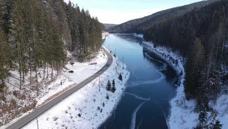 Flying-over-frozen-lake,-following-a-car-approaching-the-Linachtalsperre-dam