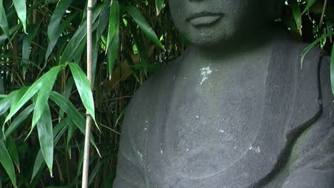 Tilt-up-from-hands-to-face-of-statue-of-Jizo-in-a-Japanese-garden