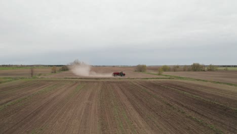 Drone-flying-low-and-fast-over-farm-field-toward-vehicle-spreading-fertilizer-with-dust-coming-from-wheels