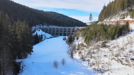 Low-aerial-approach-of-the-Linachtalsperre-dam-in-Black-Forest,-Germany-with-snow