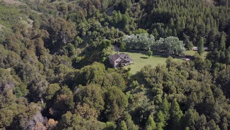Aerial-shot-of-luxury-stone-villa-surrounded-by-beautiful-nature-forest-during-sunny-day-in-Patagonia,-Argentina