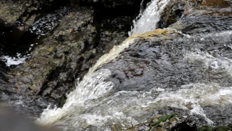Macro-shot-of-natural-rugged-waterfall-pouring-over-brown-rocks-and-cascading-down-mountain-river-in-rugged-outdoor-environment
