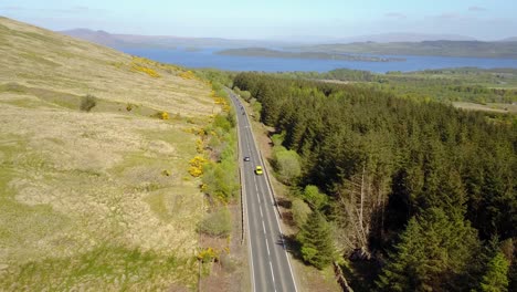 Aerial-forward-over-Scottish-road-and-Lomond-lake-in-background,-Lowlands-in-Scotland