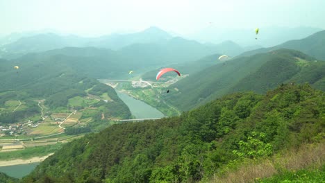 Paraglider-takes-off-from-the-mountain-and-glides-towards-Danyang-city,-South-Korea,-sunny-and-vivid-colors-following-shot