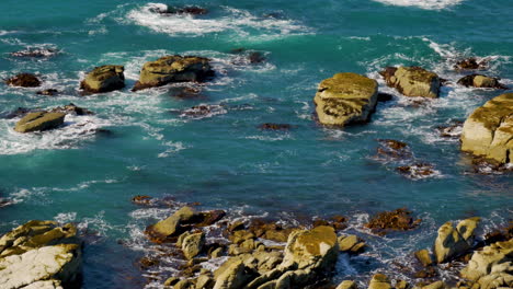 Slow-motion-shot-of-waves-of-Pacific-ocean-crashing-against-outstanding-rocks-during-summer-light