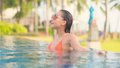 Woman-wearing-large-sunglasses-relaxing-in-infinity-swimming-pool-of-beautiful-luxury-tropical-resort