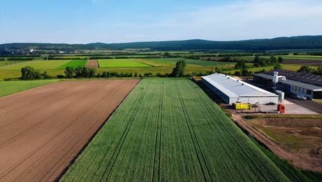 AERIAL---Beautiful-green-farm-fields-next-to-construction-site,-Austria,-wide-shot