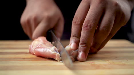 Butcher-men-cutting-raw-chicken-wings-with-a-sharp-knife-and-shaping-into-a-lollipop-on-a-chopping-board