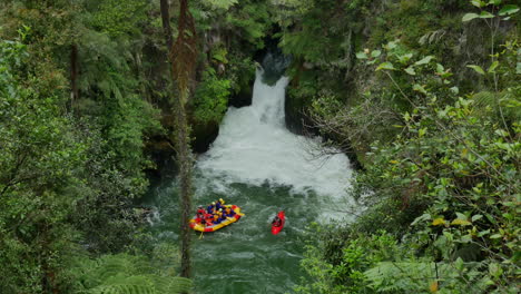 Aerial-birds-eye-shot-of-people-in-boat-during-rafting-trip-with-kayak-surrounded-by-green-wild-nature-at-Tutea-Falls