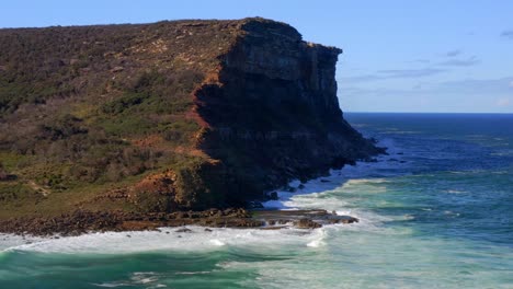 Beautiful-blue-waves-splashing-by-the-rocky-cliff---Royal-National-Park---Aerial