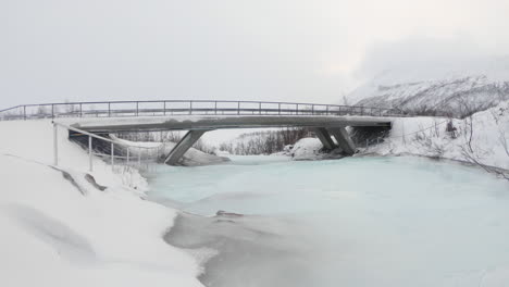 Bridge-road-over-a-frozen-river-close-to-a-waterfall-in-Björkliden,-Sweden