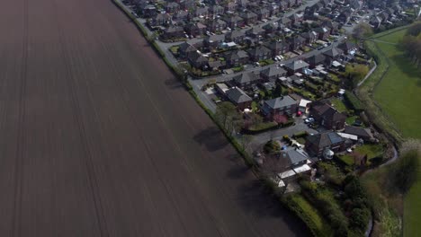 Countryside-housing-estate-aerial-view-flying-above-England-plowed-farmland-residential-community-homes
