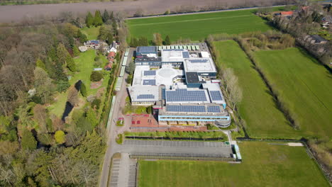 Aerial-of-large-high-school-with-solar-panels-on-rooftop---drone-flying-backwards