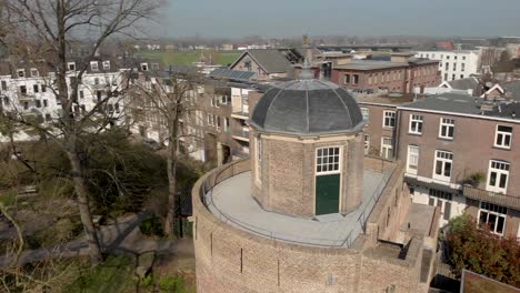 Slow-backwards-and-rotating-aerial-reveal-of-surrounding-of-historic-Bourgonje-stronghold-tower-and-city-wall-in-Zutphen,-The-Netherlands,-against-a-blue-sky