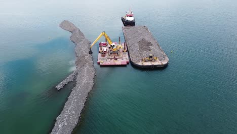 Excavadora-En-Barcaza-En-Agua-Construyendo-Rompeolas-De-Rocas-Cerca-De-La-Costa