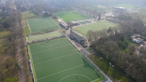 Aerial-of-green-soccer-and-hockey-fields-at-the-edge-of-a-small-town