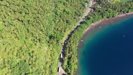 Small-Remote-Village-Road-With-Big-Trucks-Moving-Around-On-A-Tropical-Island-In-The-Philippines---aerial-top-down