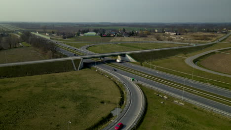 Aerial-view-of-car-traffic-on-highway-exit-ramp-with-bridge-in-rural-Cedry-Poland