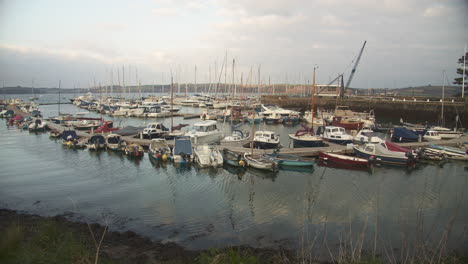 A-view-looking-across-multiple-small-moored-boats-in-Mylor-Bridge-harbour,-gentle-ripples-on-the-harbour-surface