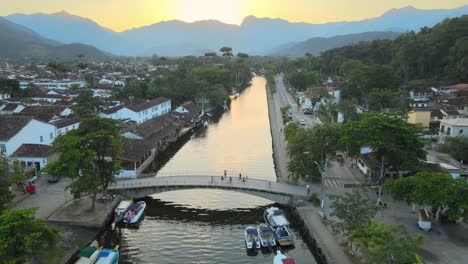 Sunset-lights-in-a-gliding-flight-over-the-river-in-the-historic-center-of-Paraty,-a-World-Heritage-Site-in-Rio-de-Janeiro,-Brazil