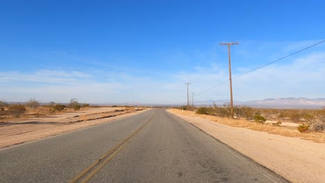 Driving-along-an-empty-road-through-the-sandy-landscape-of-the-Mojave-Desert---driver-point-of-view