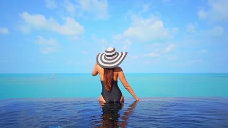 Back-of-slim-female-in-swimsuit-and-summer-hat-enjoying-in-stunning-view-on-sea-skyline-from-infinity-swimming-pool,-luxury-holiday-concept,-full-frame