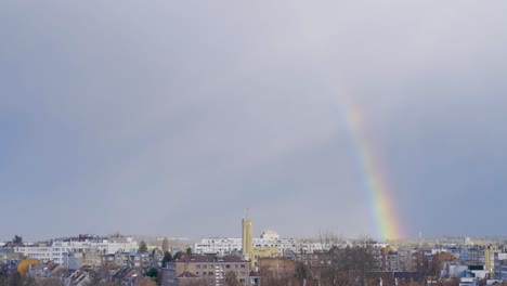 Belgian-Flag-Waving-On-Top-Of-Woluwe-Saint-Lambert-Town-Hall-In-Brussels,-Belgium,-Fading-Rainbow-In-Cloudy-Sky-Background