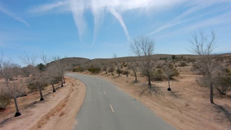 Corriendo-A-Lo-Largo-De-Una-Carretera-Rural-En-El-Desierto-De-Mojave-Con-Vistas-Desde-Un-Dron-En-Primera-Persona